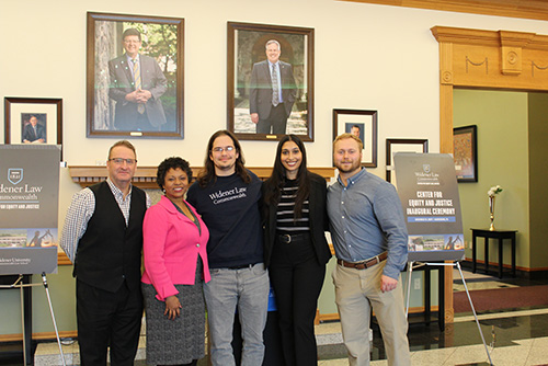 Group photo taken at the Center for Equity and Justice Inaugural Ceremony at Widener Law Commonwealth. The image shows five individuals standing together in the law school lobby, smiling for the camera. Framed portraits and event signage are visible in the background