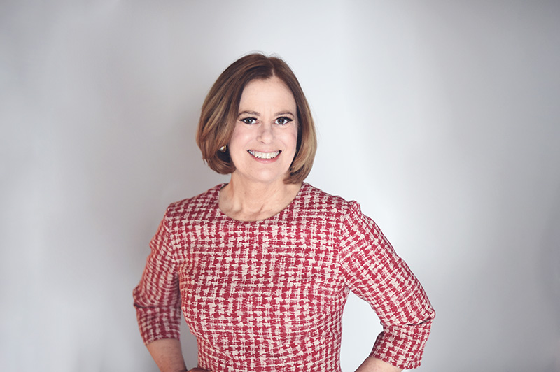 Image of Professor Juliet Moringiello. She is wearing a a red and white tweed dress with 3/4 length sleeves standing in front of a white background. 