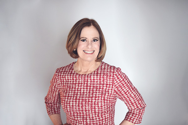 Image of Juliet Moringiello, a woman with short, styled hair, wearing a red and white patterned dress, standing against a light, neutral background.