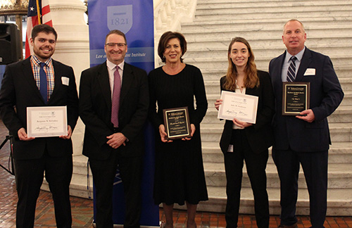 A group photo including Judge Susan Schwab, Nick Matash, Julie Stenhouse, Ben McFadden and Dean andre douglas pond cummings. Behind them is an American flag and the a Widener Law Commonwealth blue banner. 