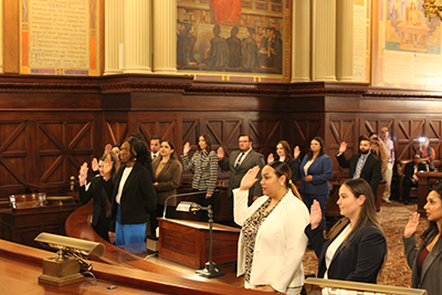 Image of alumni holding up their right hand being sworn in while standing inside the Pennsylvania Supreme Courtroom.