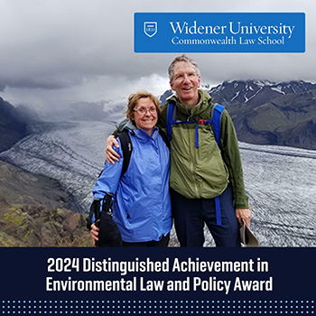 A photo of two individuals, one of them being John Dernbach, outdoors with a mountainous landscape in the background. Both are dressed in hiking gear, smiling and standing close together. The image features the Widener University Commonwealth Law School logo at the top and the text "2024 Distinguished Achievement in Environmental Law and Policy Award" below