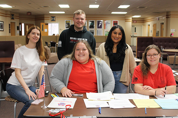 The Spirit of Service team wearing red, black and white shirts sitting at the check in table smiling for the camera. 