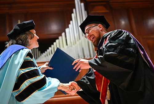 Image of student being handed degree while crossing the stage at commencement. 