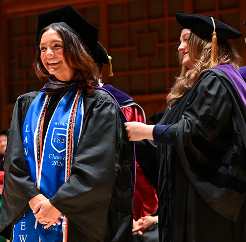 Valedictorian Kiera Flannery being hooded by her sister on stage at the forum during commencement. 