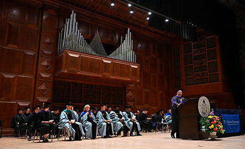 Dean andre douglas pond cummings speaking at the podium on stage at commencement