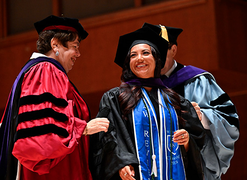 Image of student being hooded by Professor Robyn Meadows and Professor Christian Johnson