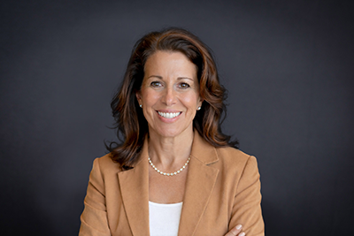Image of Christie Corado wearing a tan blazer and white shirt. She has dark brown hair. 