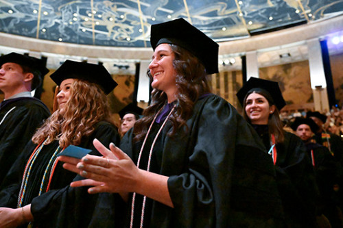 Image of graduates at commencement standing and clapping at the forum