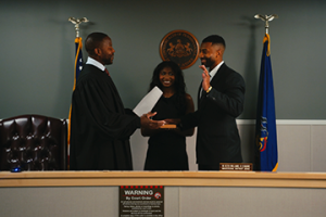 Picture of all three Williams' standing behind the judicial bench smiling at the camera. 