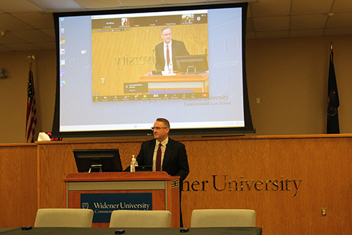 ean andre cummings of Widener Law Commonwealth speaks at the EMS symposium, with his presentation displayed on a large screen behind him.