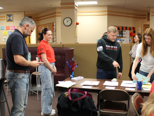 Students in red shirts gather around the check in table to help assist veterans and first responders