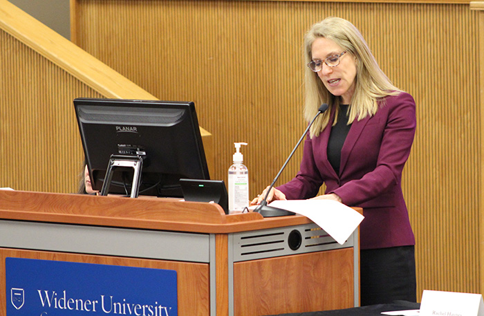 Image of Michal Buchhandler-Raphael speaking at the podium in A180 to the crowd.