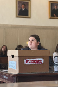 Image of Jessica Poley sitting in a courtroom behind a desk with an evidence box on top of it. 