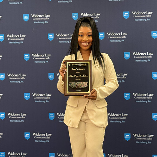 Miss-Kye Gallon stands in front of the Widener University Commonwealth Law photo screen with her award. 