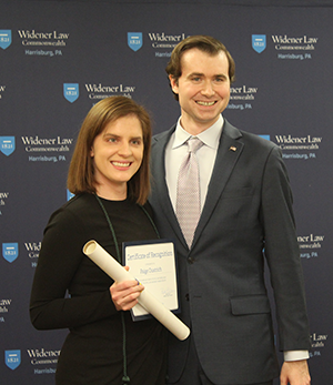 Image of David Dugan and Paige Oustrich standing before the Widener Law Commonwealth step and repeat. They are smiling and holding up their awards. 