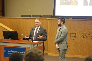 Image of Dean andre douglas pond cummings speaking at the podium awarding a plaque to Rishi Nayee
