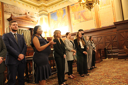 The graduates stand before the room, smiling, after they are formally sworn in. 