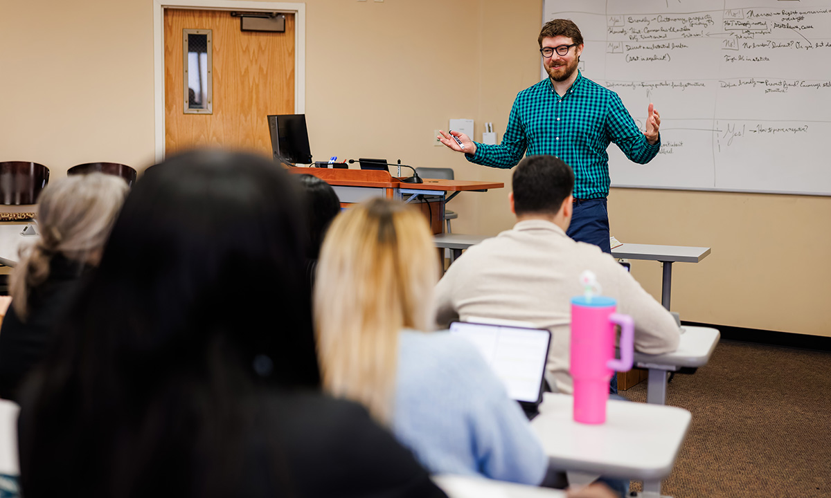 Professor Noah Chauvin teaching a class in front of a white board with notes on it.