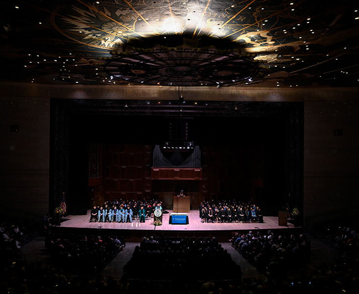 Photo of the stage at The Forum with the graduates and faculty seated.