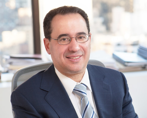 Photo of speaker; man in dark suit with tie and a light office background.