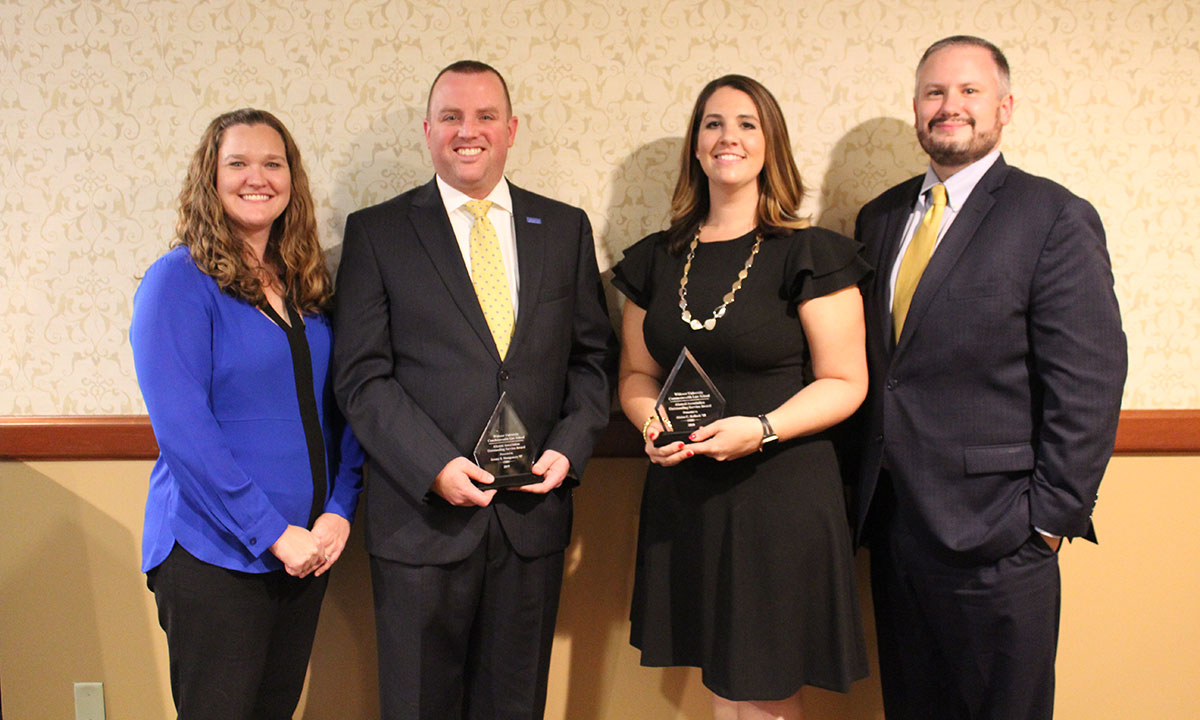 Four people pose together at a Widener Law Commonwealth alumni award ceremony, two of them holding crystal recognition trophies.