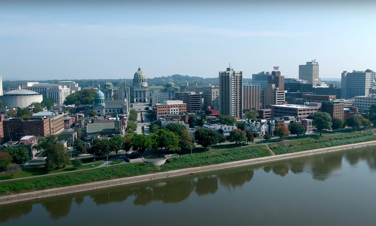 Aerial view of downtown Harrisburg along the Susquehanna River, with the Pennsylvania State Capitol dome rising above the city skyline on a clear fall day.