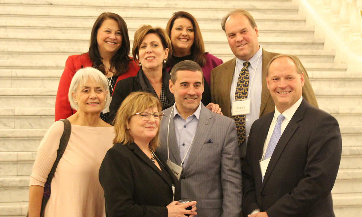 A group of Widener Law Commonwealth alumni pose together on the marble staircase of the Pennsylvania State Capitol during a 2019 alumni event.