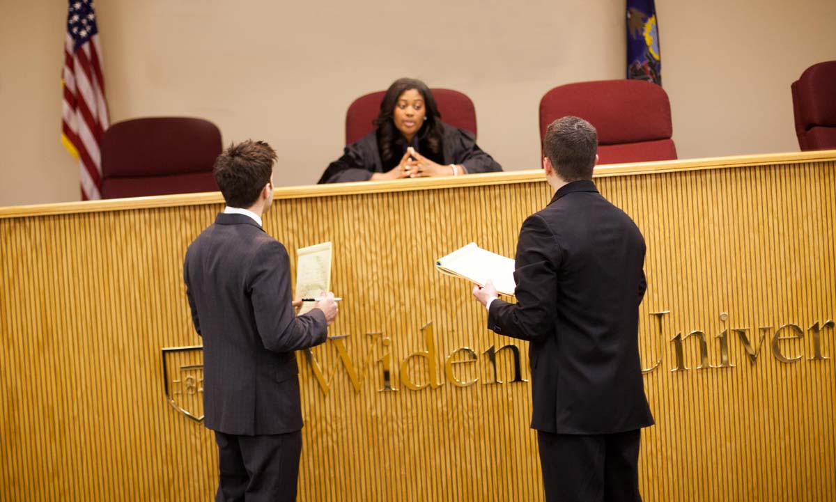 Two law students in professional suits stand before a presiding judge at a Widener University courtroom bench during a mock trial competition.