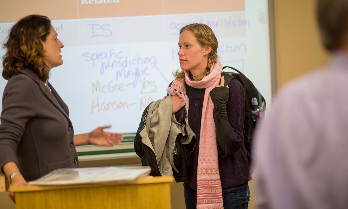 Jill Family speaks with a student after class at the front of the room, with a projected whiteboard showing jurisdiction notes visible behind them.