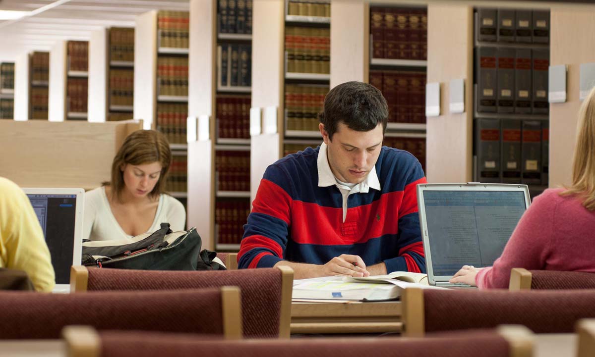 Students study independently at carrels in the campus law library, with shelves of legal volumes filling the background.