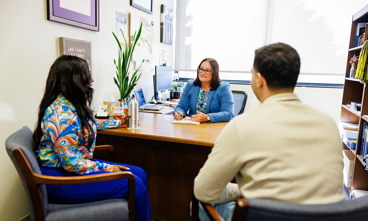 A career development staff member meets with two law students in her office, taking notes as they confer across her desk.
