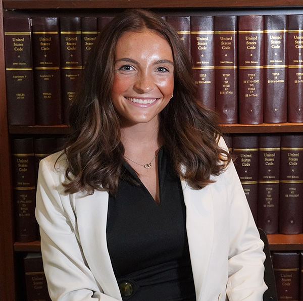 Kiera Flannery — smiling headshot in a white blazer, posed in front of law library shelves.