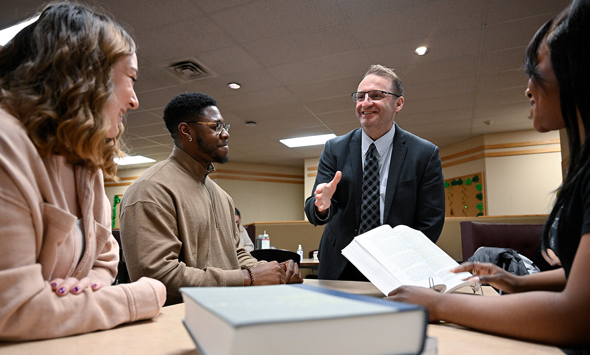 Dean andré douglas pond cummings engages with a small group of law students around a table, gesturing as he speaks, with law books open in front of them.