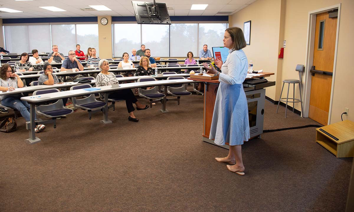 A faculty member addresses a full classroom from a podium during a Continuing Legal Education program, with attendees seated at tiered rows of desks.