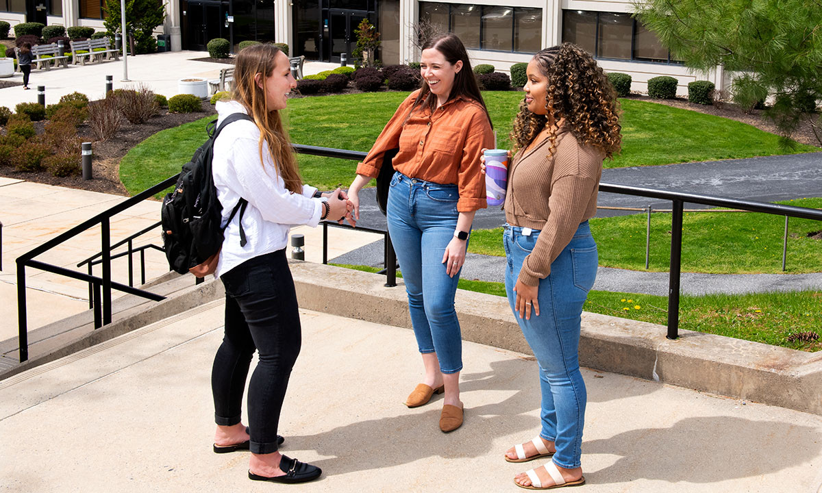 Three law students chat and laugh together on the steps outside the Widener Law Commonwealth building on a sunny spring day.