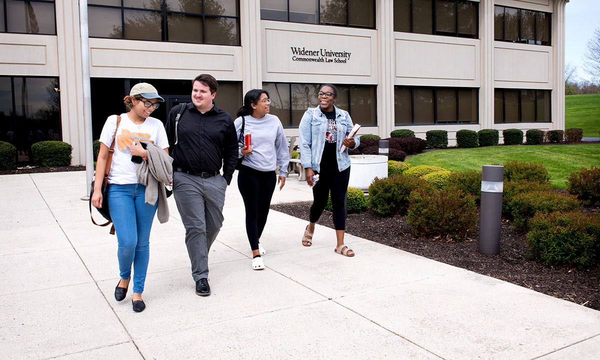 Four law students walk together along the front of the Widener University Commonwealth Law School building on a spring day.