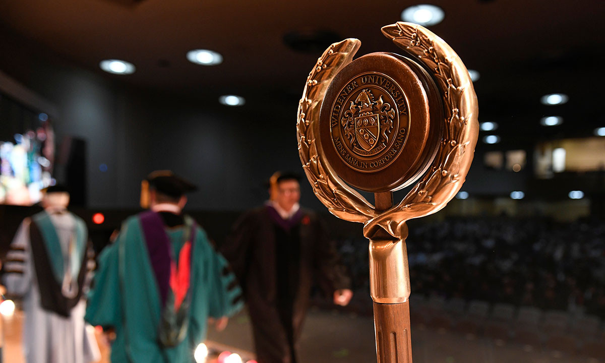 The Widener University ceremonial mace in the foreground during a commencement ceremony, with faculty in academic regalia visible in the background.