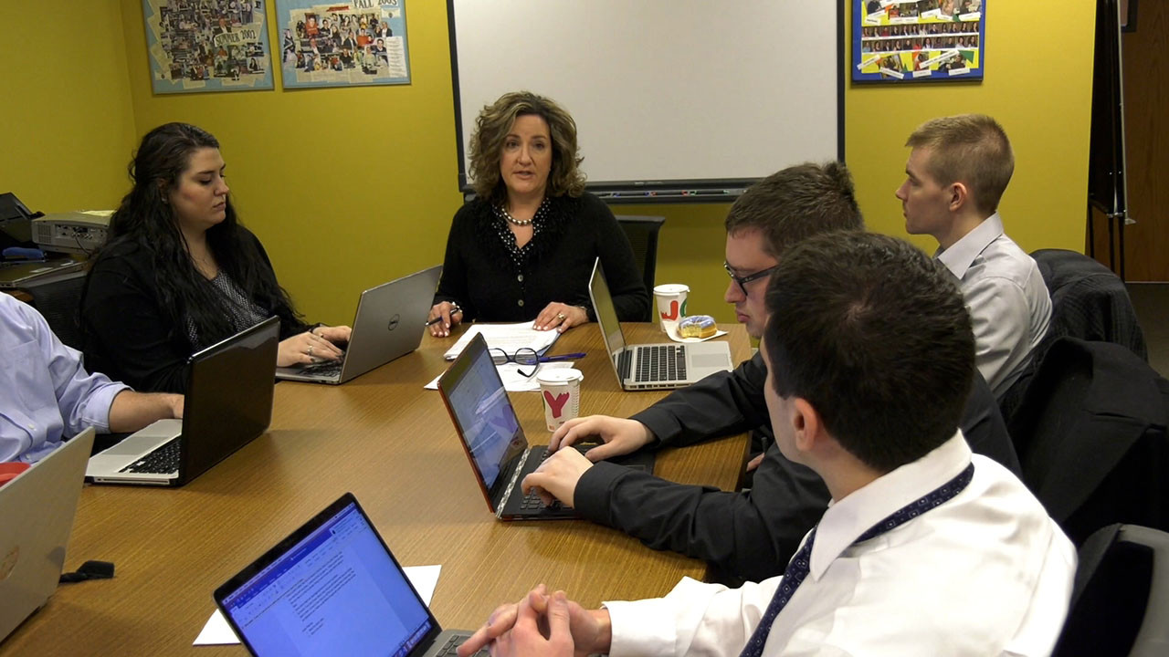 Professor Mary Catherine Scott leads a small group of law students in a conference room discussion, with students working on laptops around a large table.
