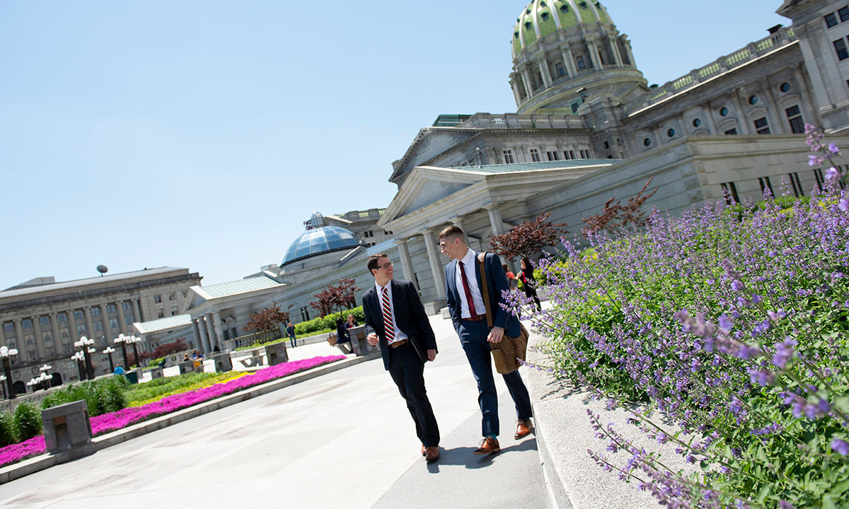 Two young men in business attire walk and converse outside the Pennsylvania State Capitol