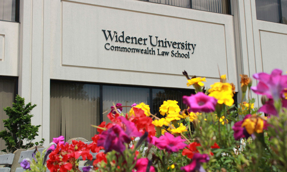 The exterior signage of the Widener University Commonwealth Law School building, framed by a colorful display of summer flowers in the foreground.