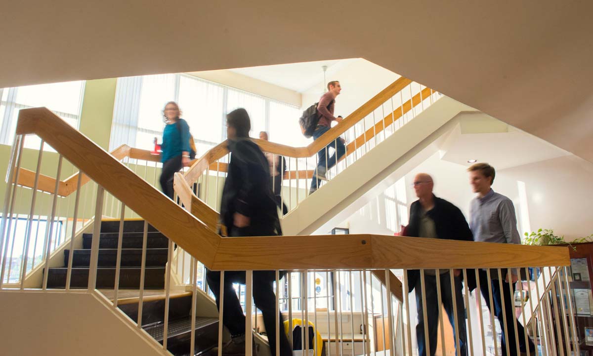 Students move through a bright, multi-level interior stairwell of the law school building, captured with a slight motion blur suggesting the bustle of a class change.