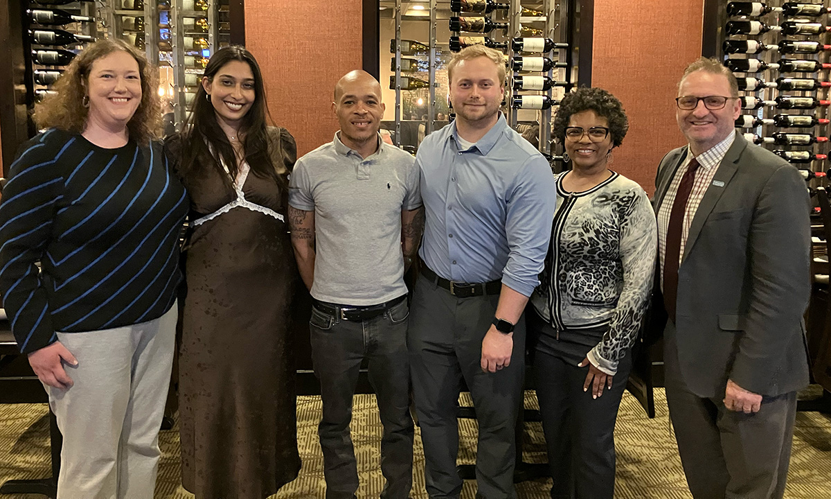 Center for Equity and Justice faculty, staff, and students pose together at a restaurant event, with wine bottle displays visible in the background.