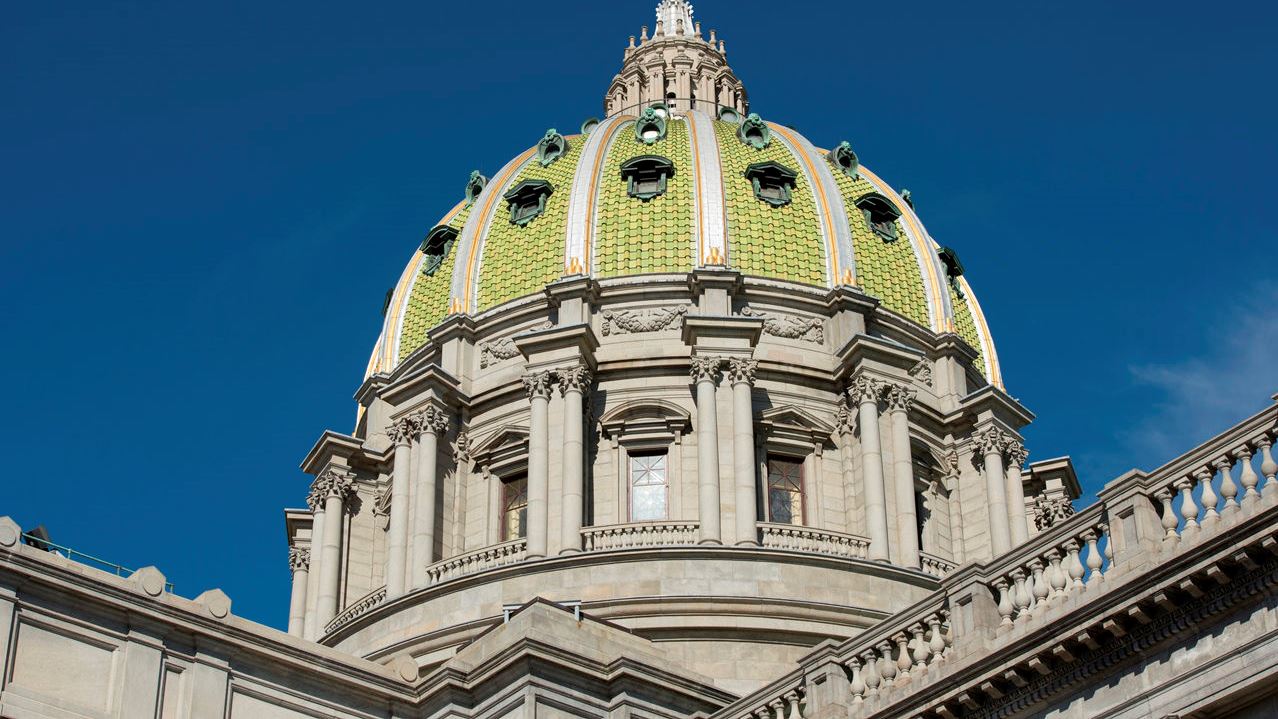 Close-up of the Pennsylvania State Capitol dome against a deep blue sky, showing the green tile and gold trim of its distinctive architecture.