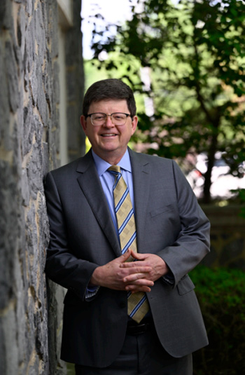 Professor Johnson in a professional headshot leaning against a tree wearing a gray suit.
