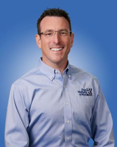 Doug Wolfberg smiles in a professional headshot, wearing a light blue button-down shirt with a Penn, Wolfberg & Wirth logo, against a blue gradient background.