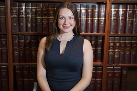 Madison Levengood — smiling headshot in a dark sleeveless dress, posed in front of law library shelves.
