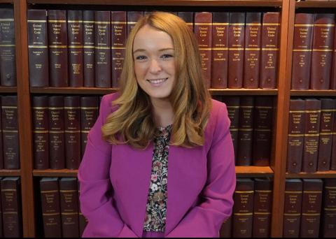 Morgan Enger: Smiling woman in a magenta blazer over a floral top, posed in front of a shelf of legal reference books.