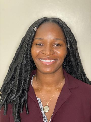 Nneoma Ibe — Smiling woman with long locs in a burgundy blazer, against a neutral background.