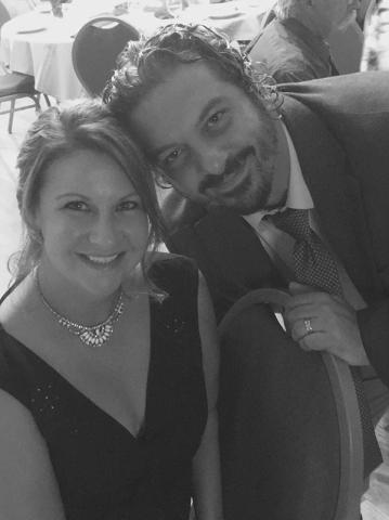 Black-and-white candid photo of George Bibikos and Kirsten Opdenhoff smiling together at a formal event.